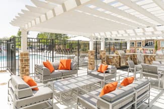 Silver furniture with grey cushions, orange pillows with pergola and pool in background
